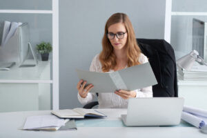 Director financiero trabajando en su despacho, en una oficina, mirando un documento mientras en su escritorio se encuentra un portátil.