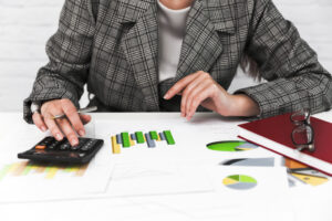 Mujer estudiando un máster en finanzas con gráficos en una mesa utilizando una calculadora